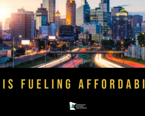 Sunset city skyline with blurred highway car lights, bold yellow text E15 IS FUELING AFFORDABILITY, MN Bio-Fuels logo bottom center.
